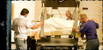 Image: Three casually dressed men preparing a dinosaur mummy for scanning.